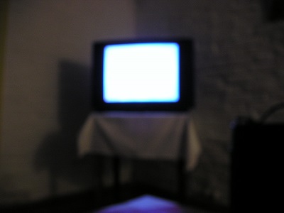 A blurred photo shows an older television on a table with a lit screen