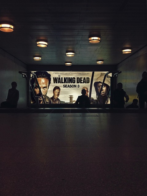 People leave a semi-lit movie theatre with an ad for The Walking Dead on the screen.