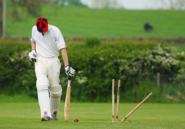 A cricket batsman walks with his head down.