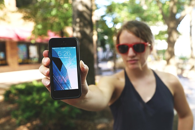 A woman wearing dark glasses holds an iPhone out to the camera