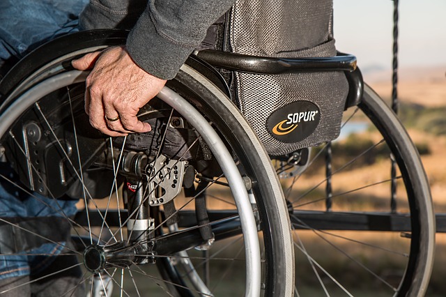A close up shot of a person in a wheelchair focusing on the wheels with a hand on the wheel closest to the camera